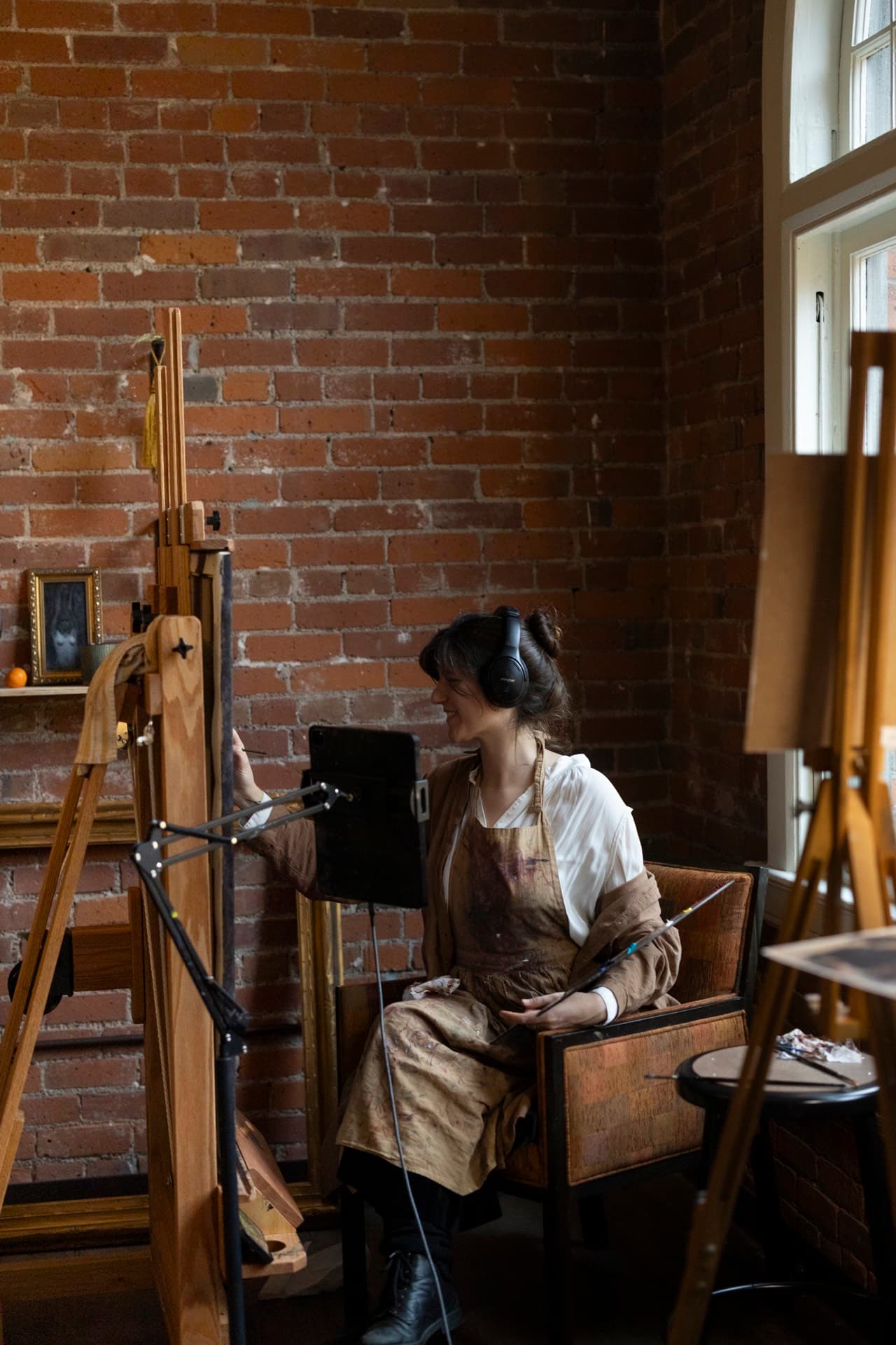 A Seattle Art Prize Fellow at her easel beside a brick wall in her third-floor Occidental studio.